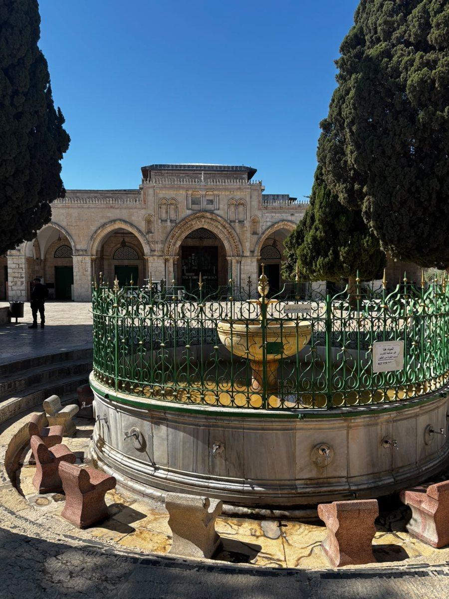 מזרקה עגולה עם גדר ירוקה מול מבנה מקושת בהר הבית